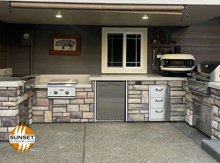 Outdoor kitchen with white countertops, grill, pizza oven and more. stone brick facings in muted tones of eggplant, taupe and grey, stainless steel appliances